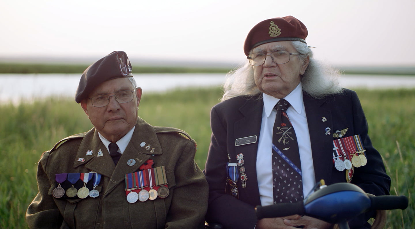 Two veterans in uniform sitting in a field / still from Cree Code Talker