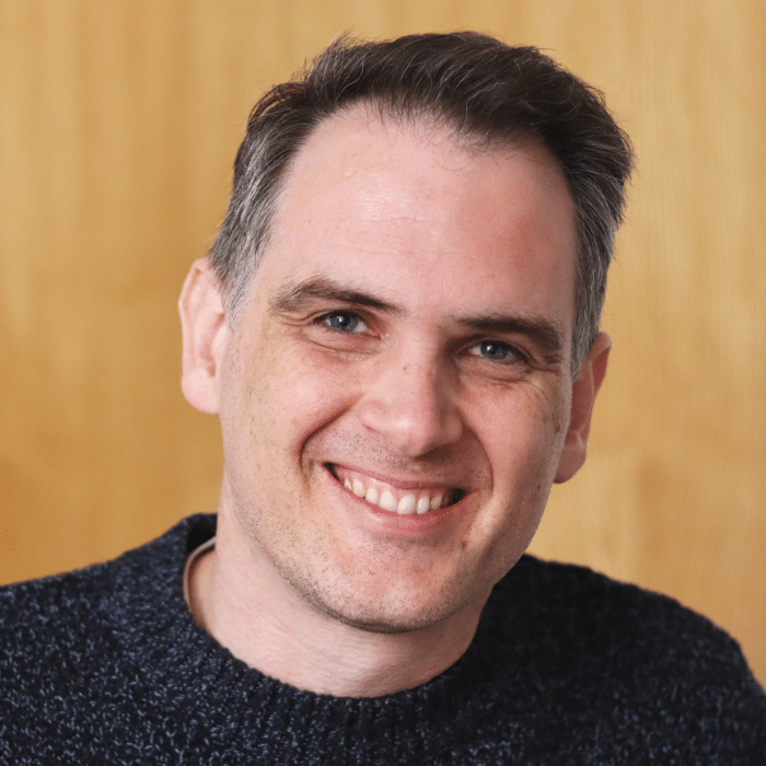 Daniel Hogg smiling with short dark hair, wearing a dark shirt.