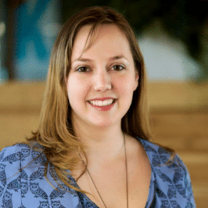 Elise Graham with long blonde-brown hair, wearing a long necklace and a blue patterned shirt.