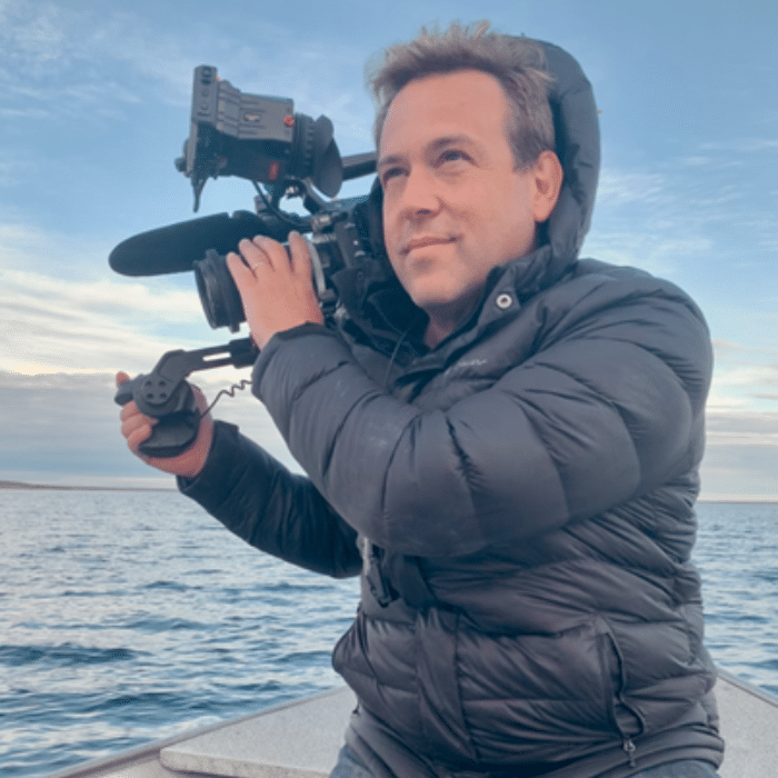 Frederick Kroetsch with short, brown hair, holding a video camera, wearing a black puffy, hooded winter coat.