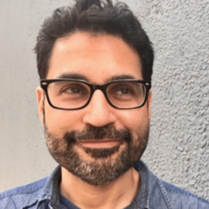 Jason Margolis with dark hair, moustache and beard wearing glasses and a denim collared shirt.