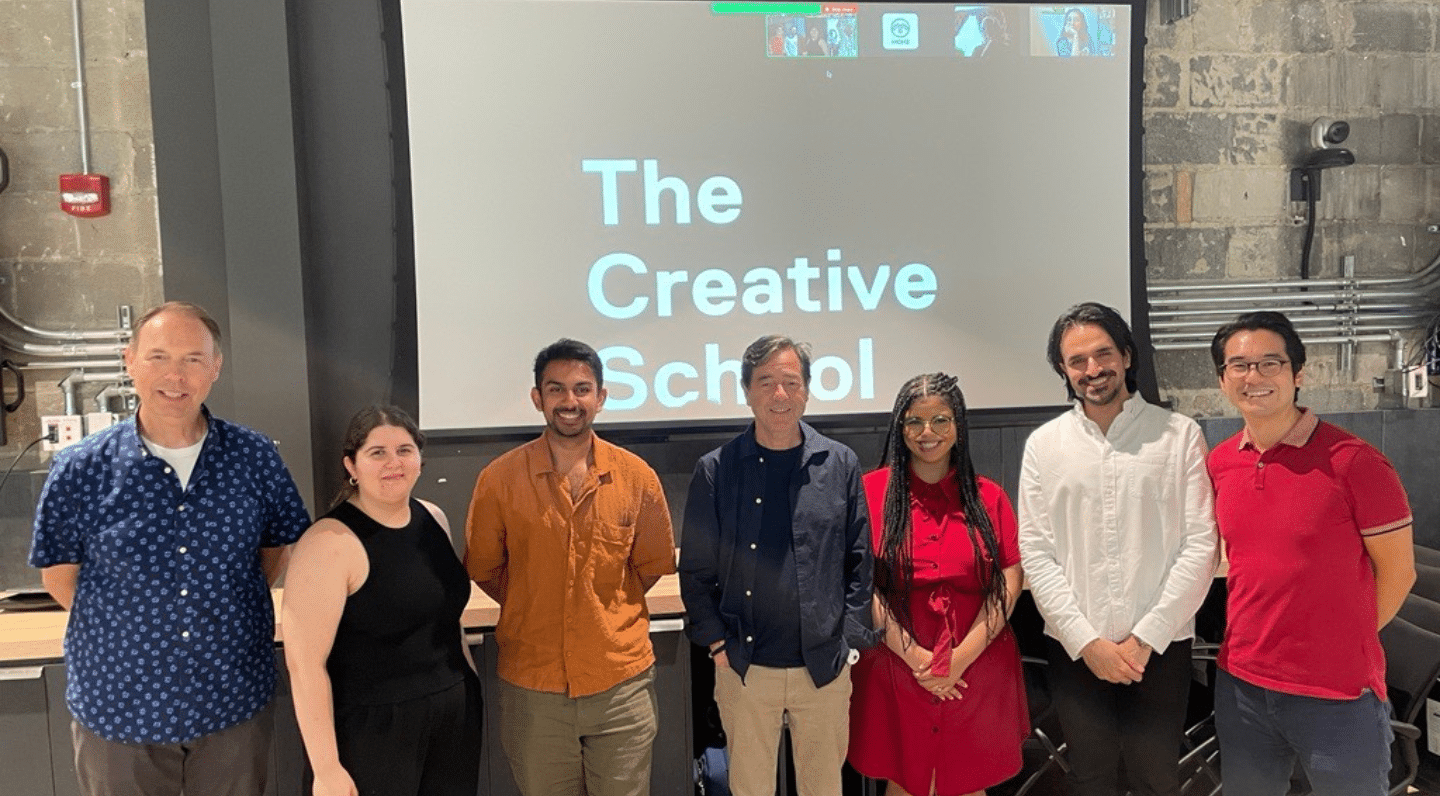 Elevate and Elevate Learning Module participants and faculty posing in front of a large screen showing, “The Creative School” in white text on a black background with additional participants in Zoom squares along the top.