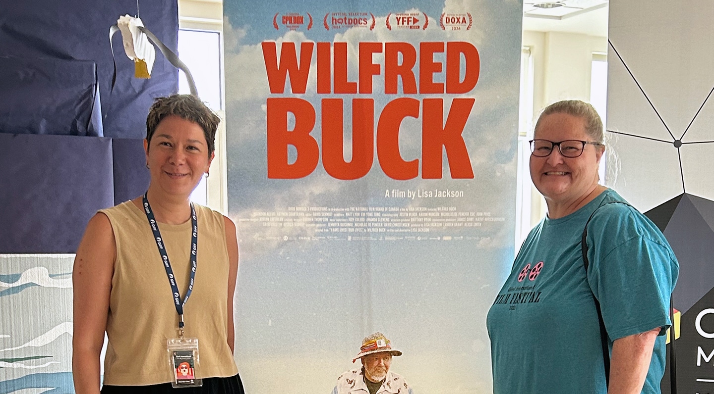 Director Lisa Jackson and National Screen Institute director of support Chris Vajcner standing on either side of a large poster for Jackson’s film, Wilfred Buck.