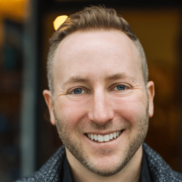 Josh Epstein with short brown hair, a short beard, wearing a grey coat.