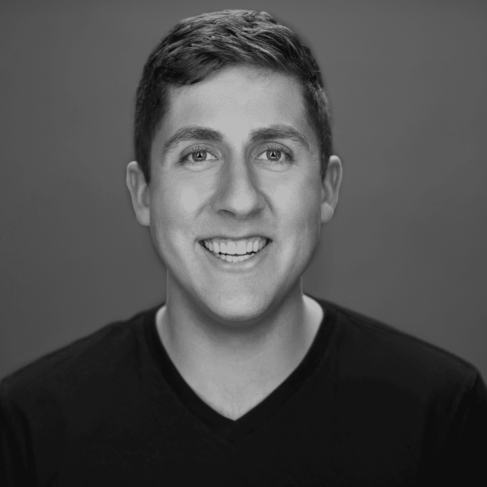 Black and white headshot of Allan. He has short hair and is wearing a black v-neck shirt.