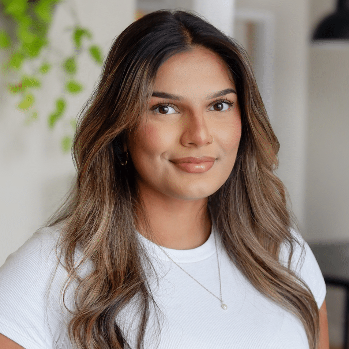 Head and shoulder portrait of a south asian woman wih long brown and blonde highlighted hair. The subject is wearing a white tshirt and smiling slightly at the camera.